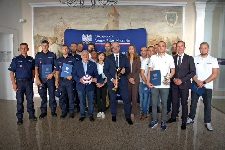 Grupa osób, w tym funkcjonariusze policji, pozuje do wspólnego zdjęcia w urzędzie Wojewody Warmińsko-Mazurskiego.