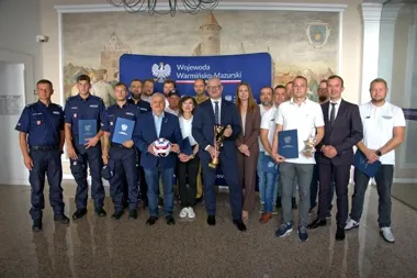 Grupa osób, w tym funkcjonariusze policji, pozuje do wspólnego zdjęcia w urzędzie Wojewody Warmińsko-Mazurskiego.