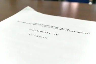 Arkusz papieru z nagłówkiem testu wiedzy dla policjantów-rzeczników dyscyplinarnych leży na drewnianym stole.