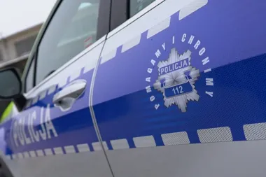 Fragment boku oznakowanego radiowozu Policji z widocznym logo i napisem „POMagamy i CHRONimy” oraz numerem alarmowym 112.