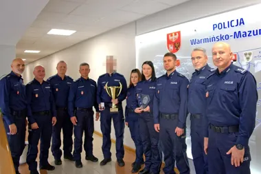 Grupa policjantów w mundurach stoi w siedzibie warmińsko-mazurskiej policji, jeden z nich trzyma puchar, a kolejna osoba statuetkę.