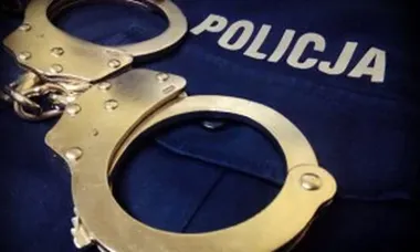 Kajdanki leżą na granatowej bluzie z napisem POLICJA.