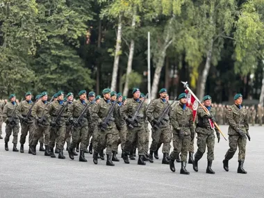 Żołnierze Wojska Polskiego w kamuflażu i zielonych beretach maszerują w szyku z bronią podczas uroczystej defilady na otwartej przestrzeni.