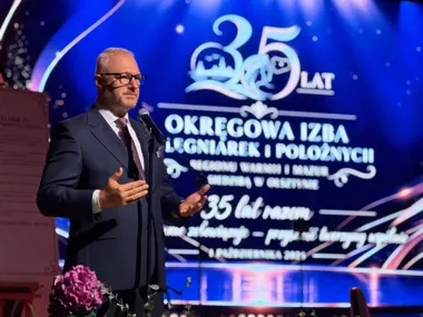 Mężczyzna w garniturze przemawia do mikrofonu podczas uroczystości 35-lecia Okręgowej Izby Pielęgniarek i Położnych w Olsztynie.