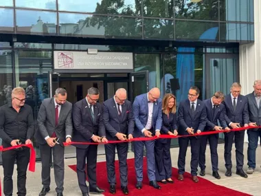 Grupa osób przecina czerwoną wstęgę podczas otwarcia siedziby Warmińsko-Mazurskiej Okręgowej Izby Inżynierów Budownictwa.