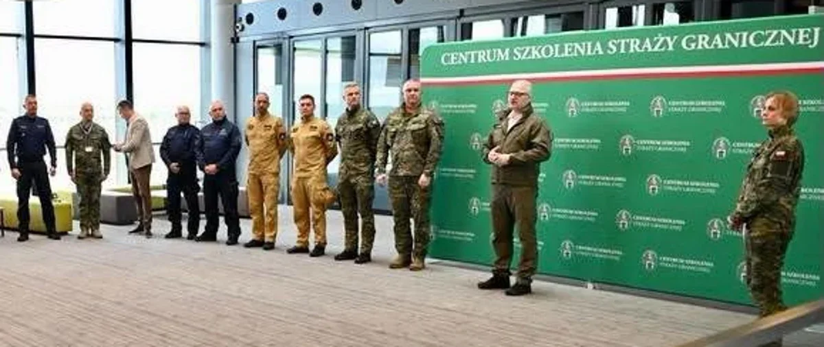 Grupa funkcjonariuszy i oficerów w mundurach oraz osób w cywilnych ubraniach stoi przed banerem Centrum Szkolenia Straży Granicznej podczas oficjalnego wydarzen