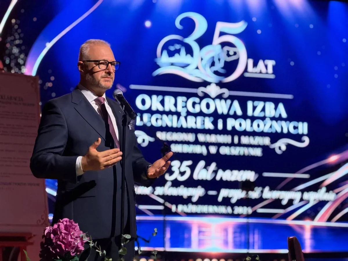 Mężczyzna w garniturze przemawia do mikrofonu podczas uroczystości 35-lecia Okręgowej Izby Pielęgniarek i Położnych w Olsztynie.
